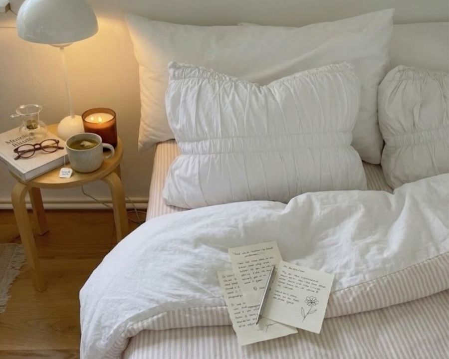 Good sleep hygiene habits in a bed with light material sheets, and bedside table with book, light and tea